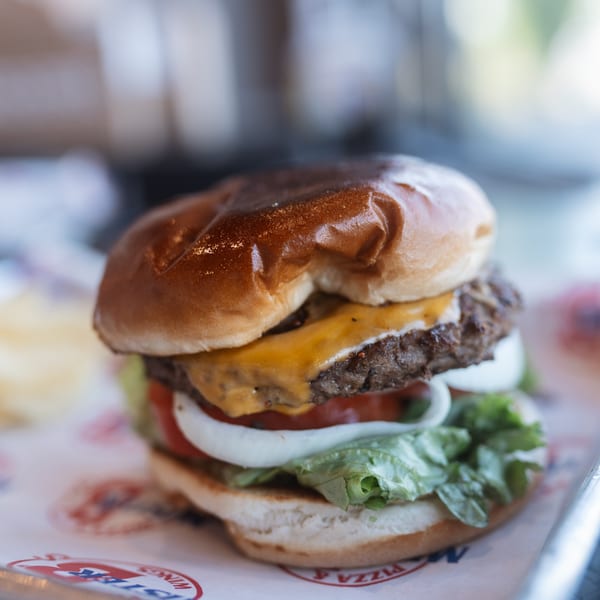 A Mister B's cheeseburger with lettuce, tomato, and onion on a branded paper liner.