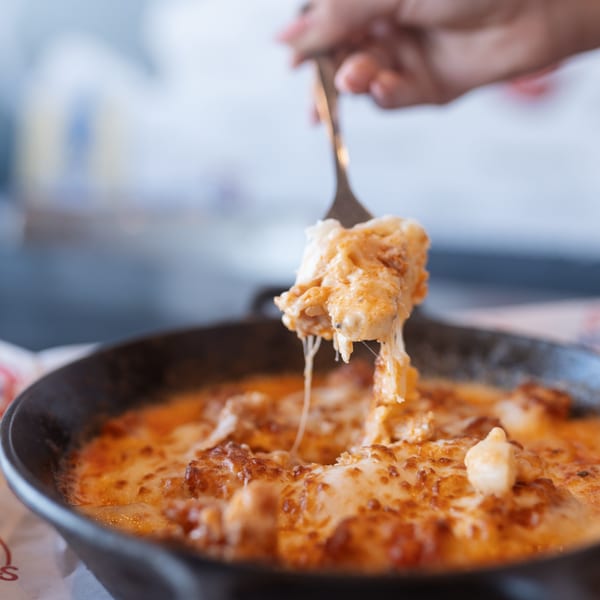 A fork lifts cheesy, saucy pasta from a black skillet, with cheese strings stretching.