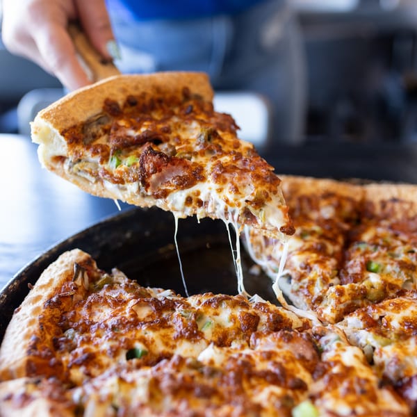 A hand lifts a slice of Mister B's pizza with melted cheese stretching from the pan.