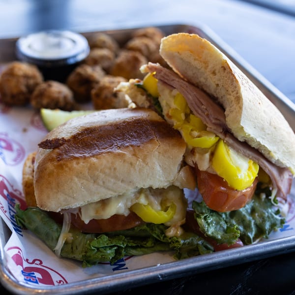 A Mister B's sandwich with meat, cheese, lettuce, tomatoes, and peppers, served with fried sides.
