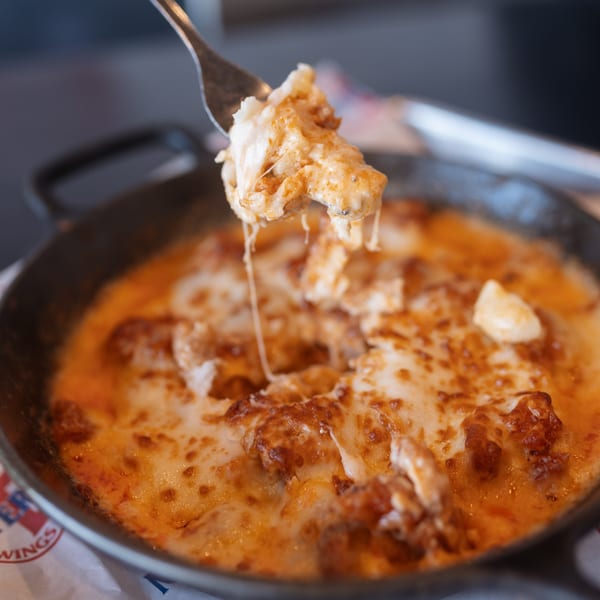 Fork lifting cheesy, saucy chicken from a skillet, with cheese strings stretching.