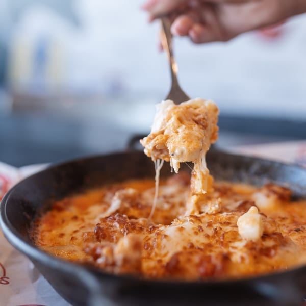A fork lifts a cheesy, saucy bite from a sizzling skillet of Mister B's mac and cheese.