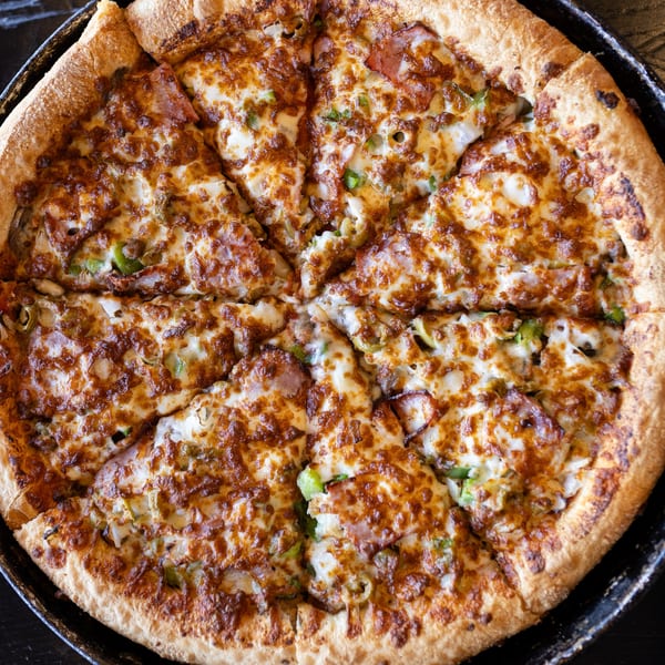 A freshly baked Mister B's pizza, cut into slices, with melted cheese and various toppings.