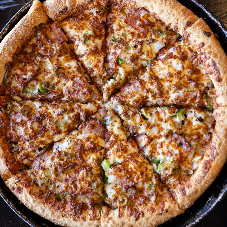A freshly baked Mister B's pizza, cut into slices, with melted cheese and various toppings.
