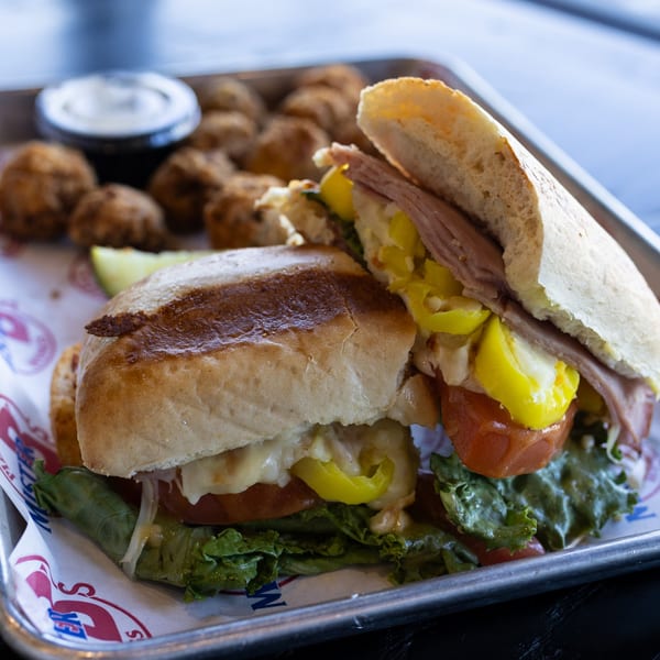 A Mister B's sub sandwich with lettuce, tomato, and peppers, served with fried appetizers.