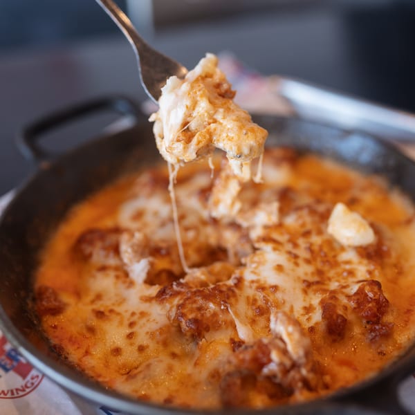 A fork lifts a cheesy, saucy bite from a hot skillet of Mister B's Pizza & Wings' baked dish.