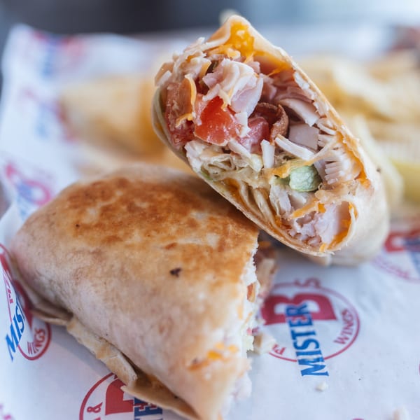 Two Mister B's chicken wraps, one cut in half, revealing chicken, cheese, and tomatoes.