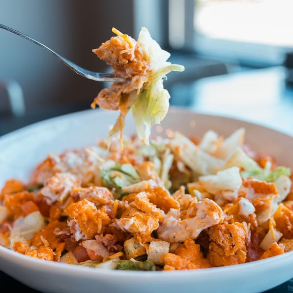 A fork lifts a bite of Mister B's buffalo chicken salad with lettuce, cheese, and dressing.