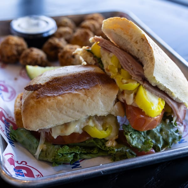 A Mister B's sub sandwich with meat, cheese, lettuce, tomatoes, and peppers, served with fried sides.