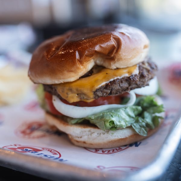 A Mister B's cheeseburger with lettuce, tomato, and onion on a branded paper liner.