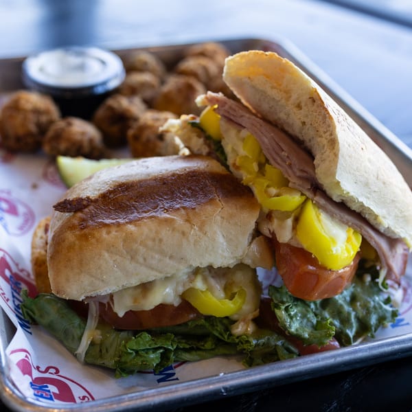 A Mister B's sub sandwich with meat, cheese, lettuce, tomatoes, and peppers, served with fried sides.