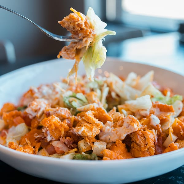 Fork lifting a piece of lettuce and buffalo chicken from a Mister B's Pizza & Wings salad.