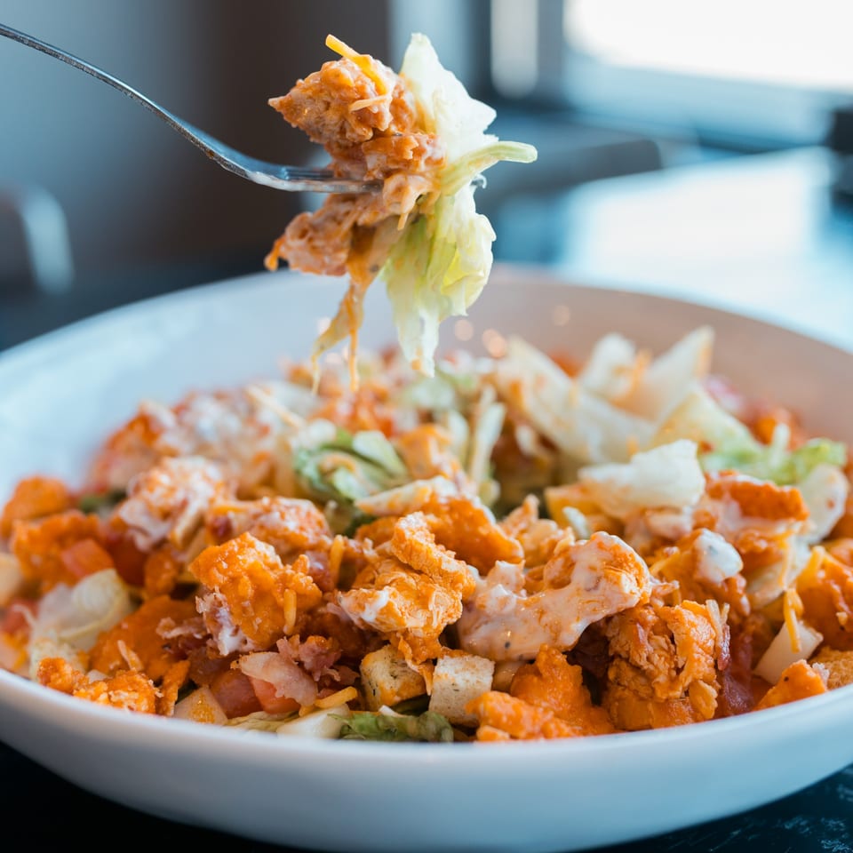 Fork lifting a piece of lettuce and buffalo chicken from a Mister B's Pizza & Wings salad.